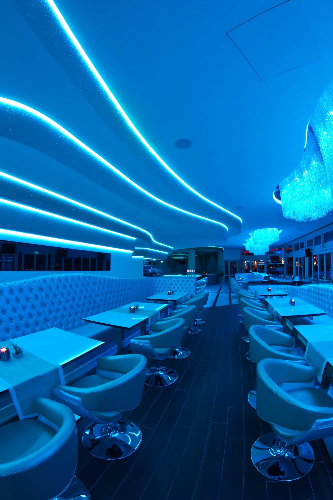 Lounge des MIO Berlin in blauem Licht mit Kristall-Kronleuchter und langen Sitzreihen