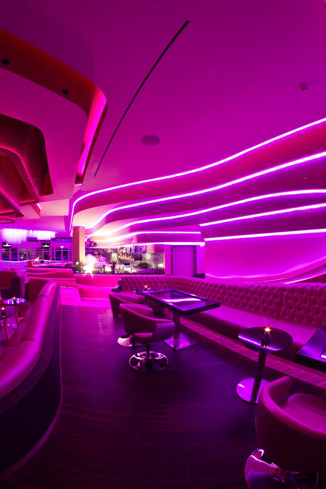 Lounge des MIO Berlin in magentafarbenem Licht mit geschwungenen LED-Linien an der Decke